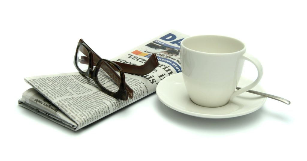 newspaper with eye glasses set on top and a cup of coffee